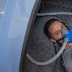 Person receiving hyperbaric oxygen therapy (HBOT) in a chamber while breathing through an oxygen mask.