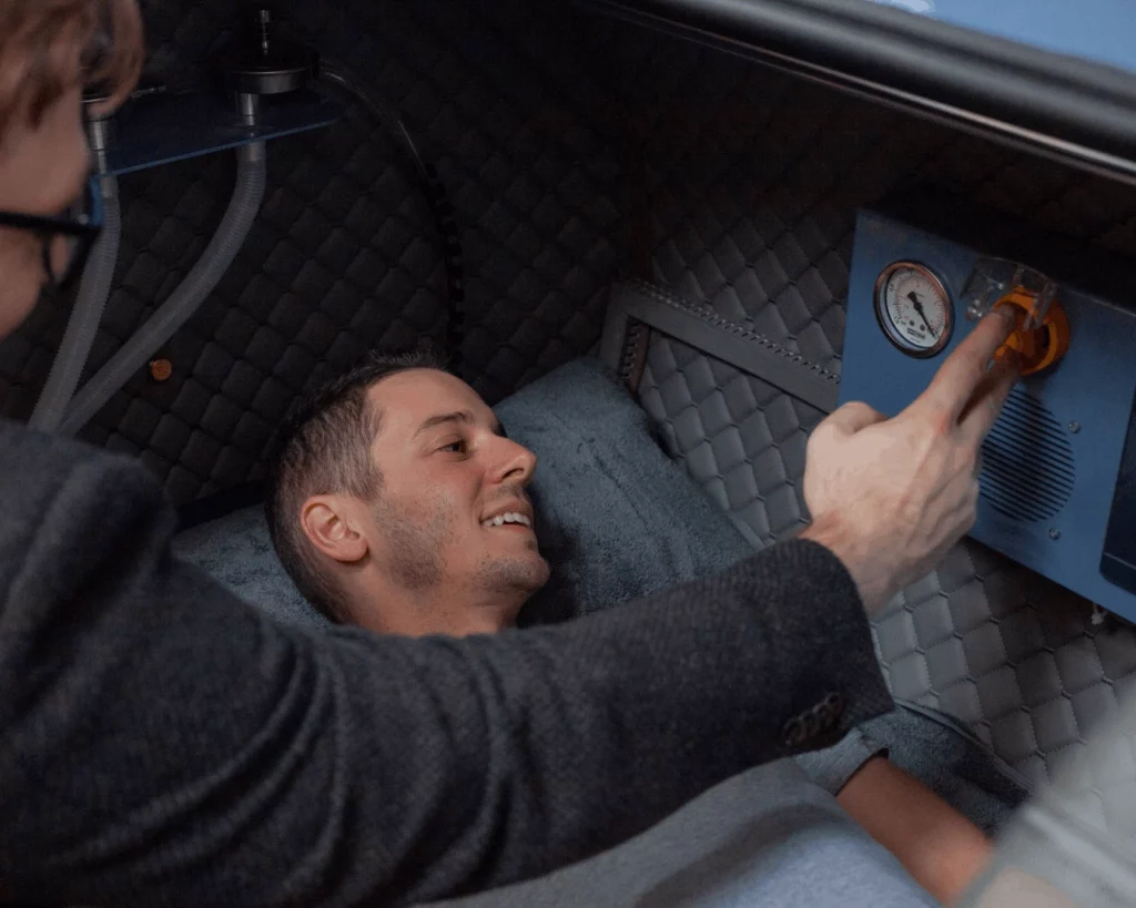 Technician assisting a patient inside a hyperbaric oxygen therapy (HBOT) chamber during treatment setup.